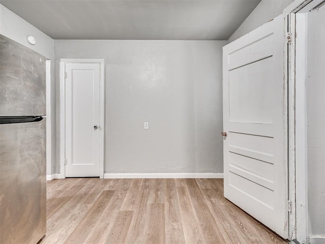 unfurnished bedroom with light wood-type flooring and stainless steel refrigerator