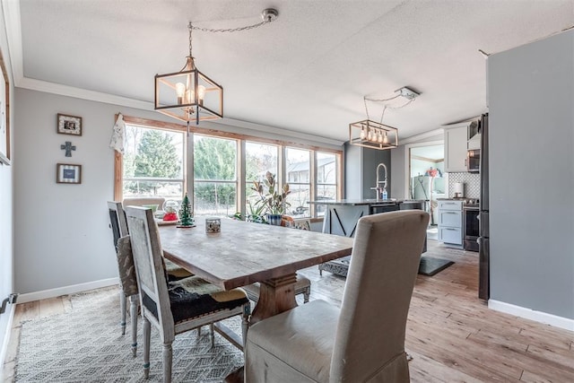 dining area featuring a chandelier, a textured ceiling, light wood-type flooring, and ornamental molding