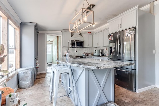 kitchen featuring hanging light fixtures, tasteful backsplash, crown molding, an island with sink, and appliances with stainless steel finishes