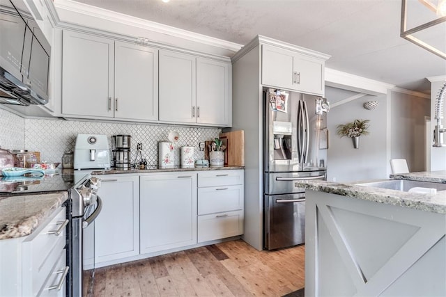 kitchen featuring light stone counters, light wood-type flooring, decorative backsplash, appliances with stainless steel finishes, and ornamental molding