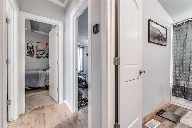 hall with crown molding, vaulted ceiling, and light wood-type flooring