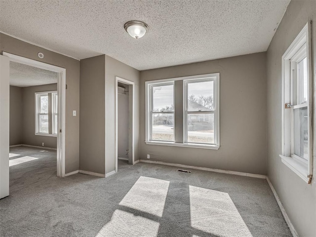 unfurnished bedroom with light carpet, a textured ceiling, and multiple windows