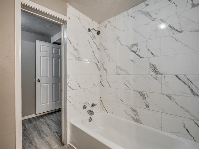 bathroom with wood-type flooring, a textured ceiling, and tiled shower / bath