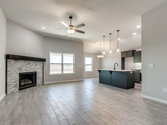 kitchen featuring ceiling fan with notable chandelier, a fireplace, open floor plan, light countertops, and light wood finished floors