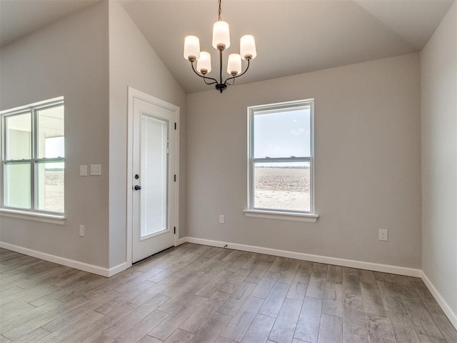 interior space featuring a chandelier, a wealth of natural light, vaulted ceiling, and wood finished floors