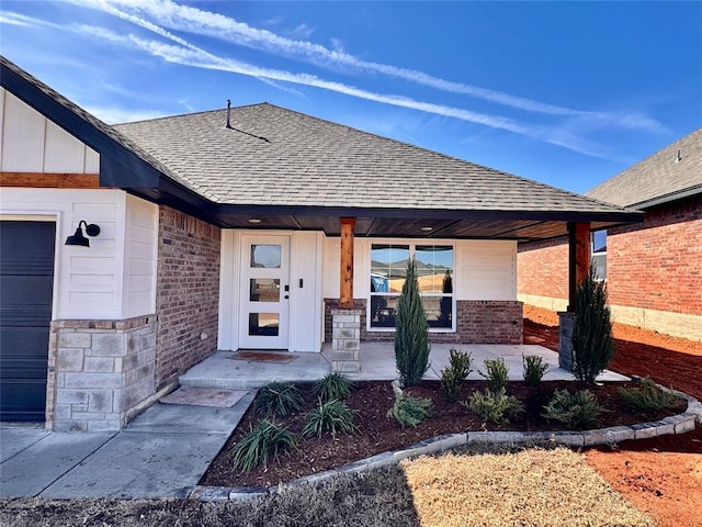 entrance to property with a garage, covered porch, a shingled roof, and brick siding