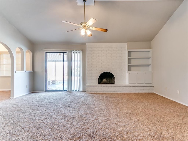 unfurnished living room featuring carpet flooring, built in shelves, a brick fireplace, and ceiling fan