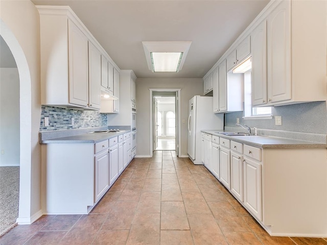 kitchen featuring backsplash, white cooktop, sink, light tile patterned floors, and white cabinets