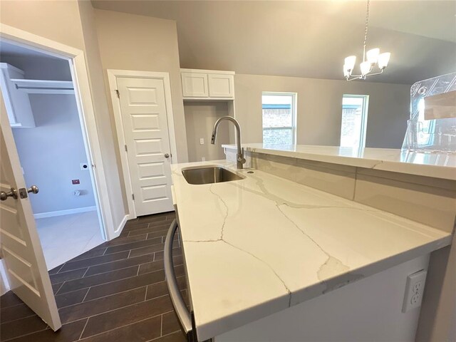 kitchen with pendant lighting, white cabinetry, vaulted ceiling, and sink