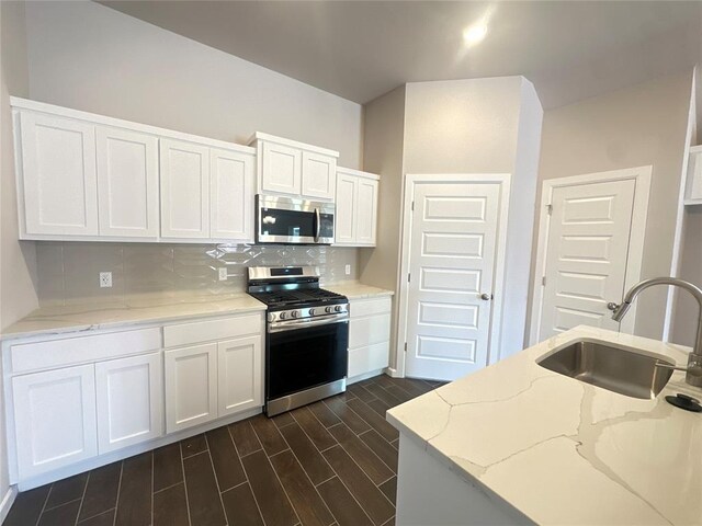 kitchen with dark hardwood / wood-style flooring, light stone counters, stainless steel appliances, sink, and white cabinets