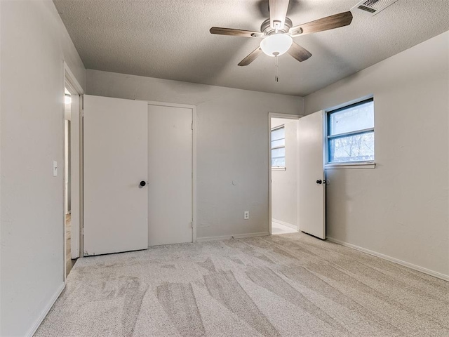 unfurnished bedroom featuring ceiling fan, light colored carpet, and a textured ceiling