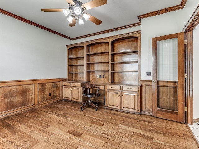 unfurnished office featuring built in desk, light hardwood / wood-style flooring, ceiling fan, and crown molding