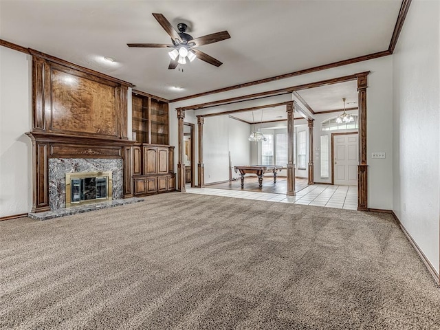 unfurnished living room with light carpet, ornate columns, ceiling fan with notable chandelier, crown molding, and a fireplace