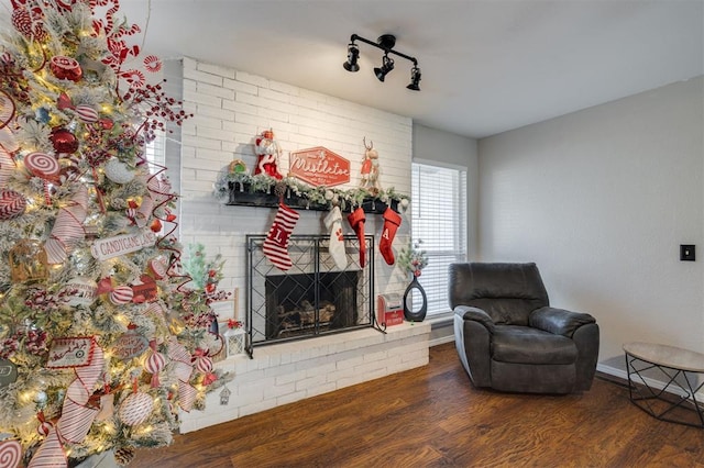 living area featuring track lighting, dark hardwood / wood-style floors, and a brick fireplace