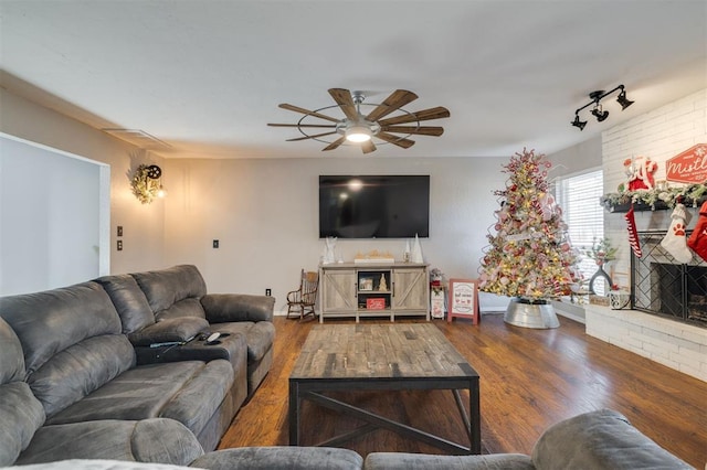 living room with track lighting, ceiling fan, wood-type flooring, and a brick fireplace