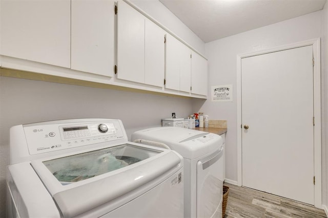 laundry area featuring cabinets, washing machine and clothes dryer, and light hardwood / wood-style flooring