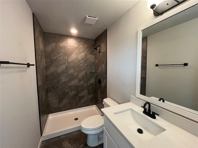 bathroom featuring a tile shower, vanity, and toilet