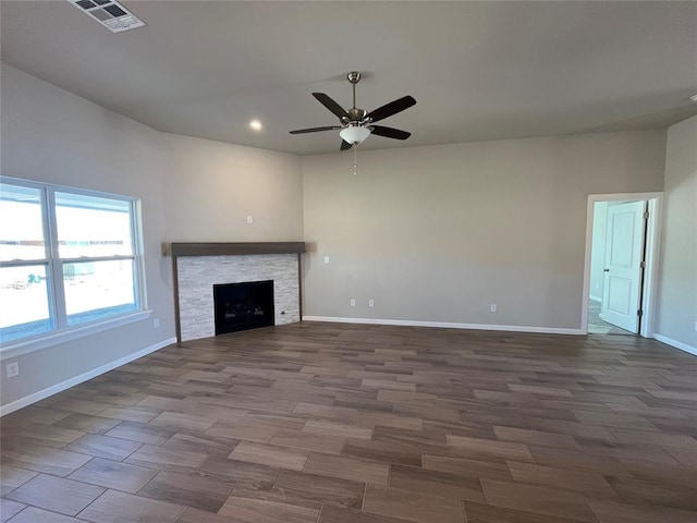 unfurnished living room with a stone fireplace, wood finished floors, a ceiling fan, visible vents, and baseboards