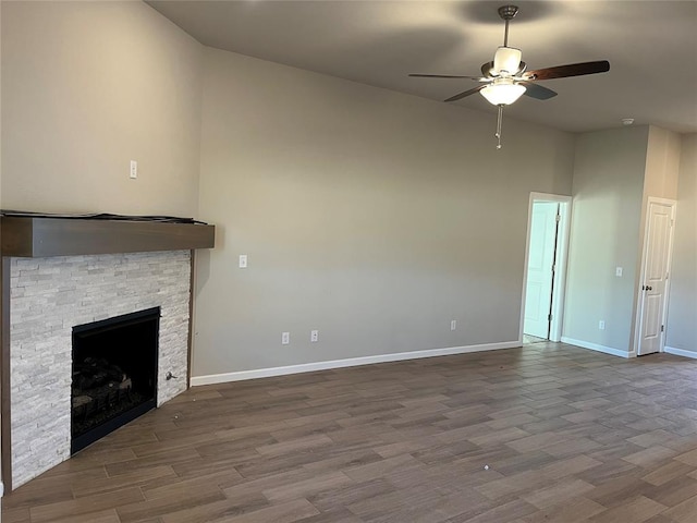 unfurnished living room with a stone fireplace, dark wood-style flooring, and baseboards