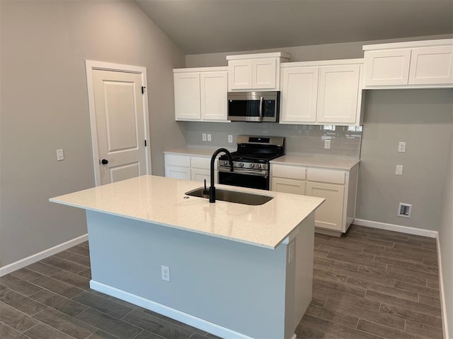 kitchen with appliances with stainless steel finishes, dark hardwood / wood-style flooring, a kitchen island with sink, sink, and white cabinetry