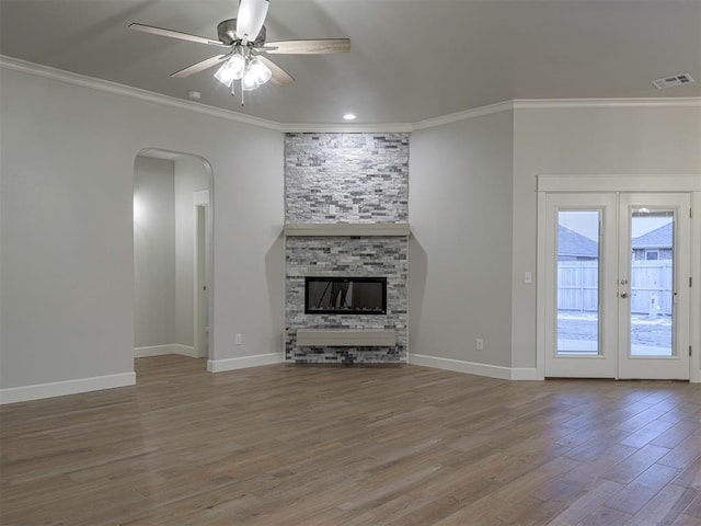 unfurnished living room with ceiling fan, french doors, crown molding, a fireplace, and hardwood / wood-style flooring