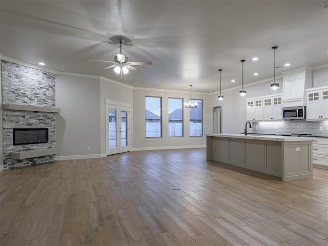 kitchen with white cabinets, ceiling fan with notable chandelier, a stone fireplace, a spacious island, and decorative light fixtures