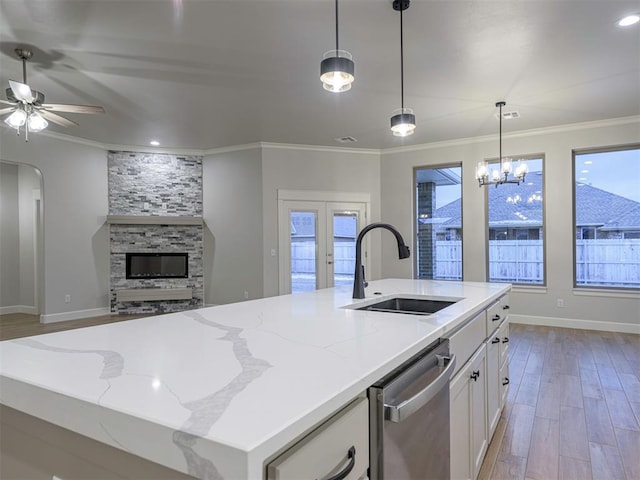 kitchen featuring light stone countertops, stainless steel dishwasher, sink, a center island with sink, and white cabinets