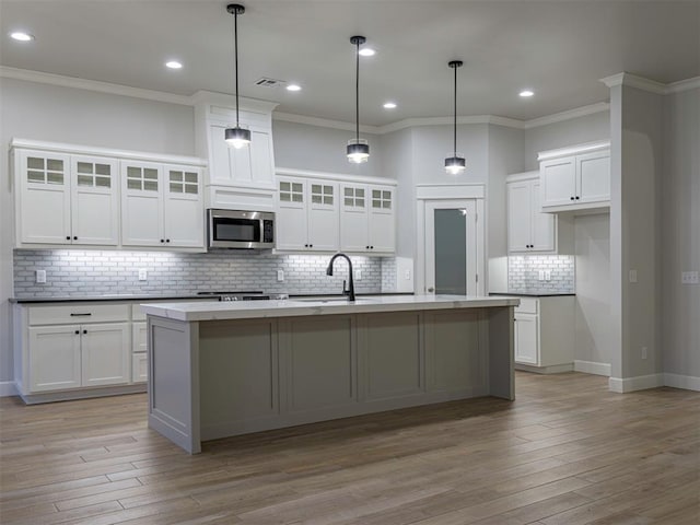 kitchen with a center island with sink, crown molding, white cabinets, and backsplash