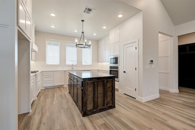 kitchen with dark brown cabinetry, white cabinetry, decorative light fixtures, appliances with stainless steel finishes, and a kitchen island