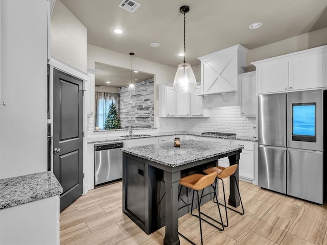 kitchen featuring light stone countertops, white cabinetry, stainless steel appliances, a kitchen bar, and a kitchen island