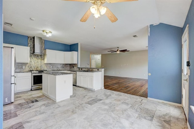 kitchen with kitchen peninsula, wall chimney exhaust hood, stainless steel appliances, a kitchen island, and white cabinetry