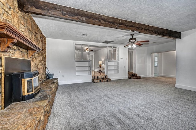 unfurnished living room with carpet flooring, a wood stove, beamed ceiling, and a textured ceiling