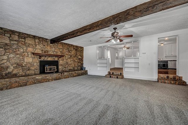 unfurnished living room with beamed ceiling, a stone fireplace, carpet floors, and a textured ceiling