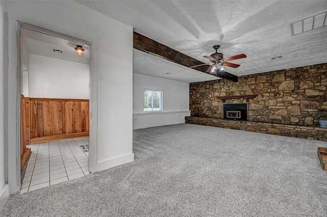 unfurnished living room with ceiling fan, a stone fireplace, a textured ceiling, and light carpet