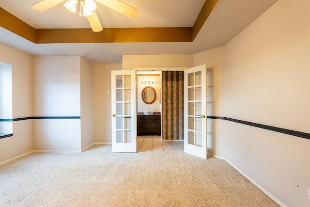 unfurnished room featuring a tray ceiling, light carpet, french doors, and ceiling fan