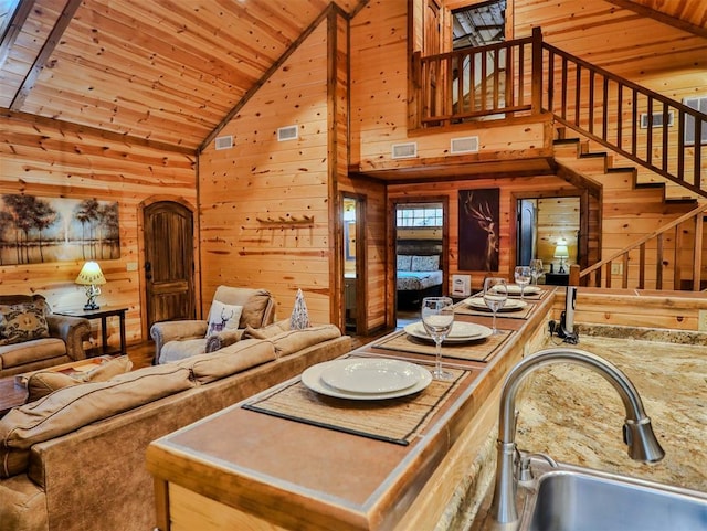 living room featuring wooden walls, sink, beam ceiling, high vaulted ceiling, and wooden ceiling