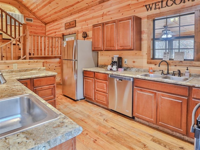 kitchen with sink, wood walls, lofted ceiling, appliances with stainless steel finishes, and light wood-type flooring