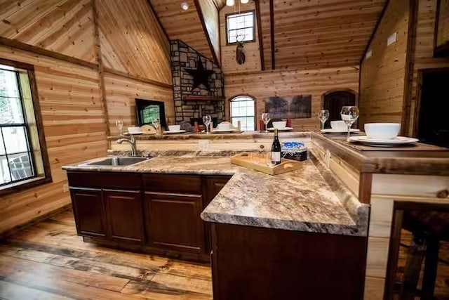 bar with high vaulted ceiling, sink, wooden walls, light hardwood / wood-style flooring, and dark brown cabinetry