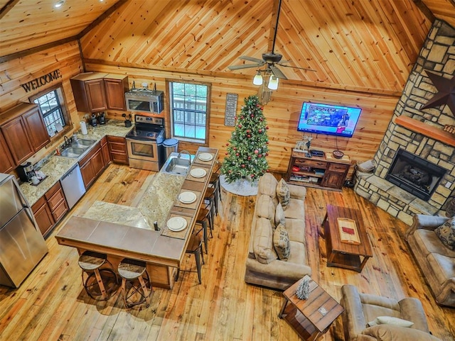 kitchen with light wood-type flooring, stainless steel appliances, high vaulted ceiling, and wooden walls