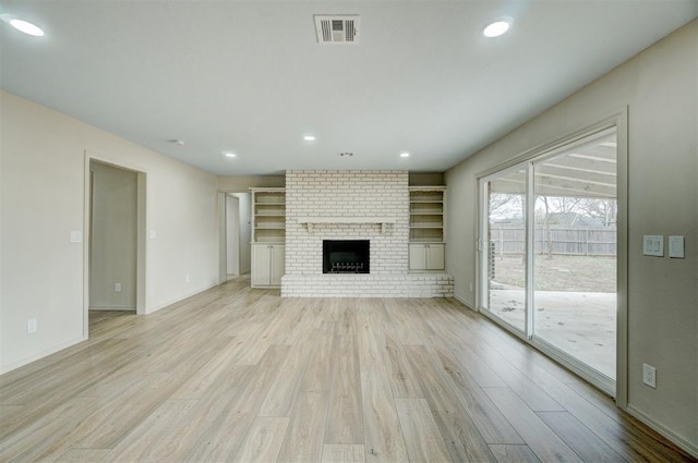 unfurnished living room featuring built in features, a fireplace, and light hardwood / wood-style flooring