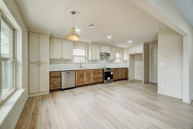 kitchen featuring appliances with stainless steel finishes, backsplash, sink, pendant lighting, and light hardwood / wood-style floors