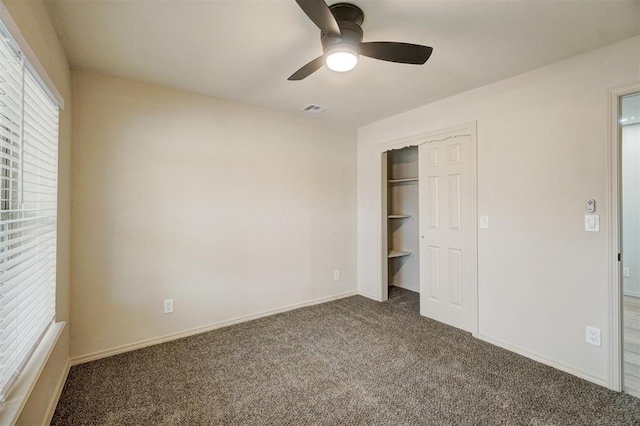 unfurnished bedroom with a closet, dark carpet, and ceiling fan