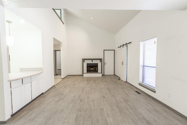 unfurnished living room featuring a barn door, high vaulted ceiling, light hardwood / wood-style flooring, and a wealth of natural light