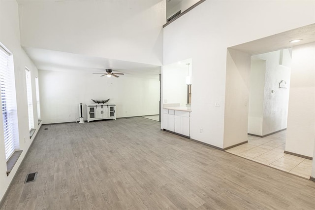 unfurnished living room with ceiling fan, a healthy amount of sunlight, light hardwood / wood-style floors, and a high ceiling