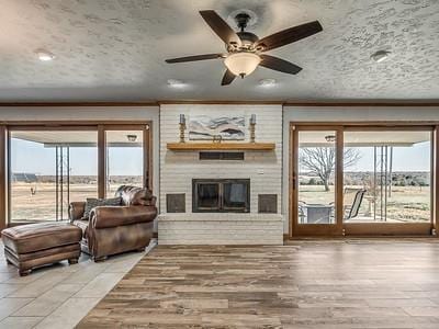 living room featuring a textured ceiling, hardwood / wood-style flooring, a brick fireplace, and ceiling fan