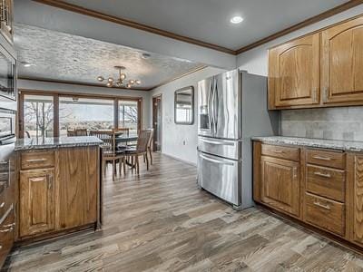 kitchen with decorative backsplash, ornamental molding, hardwood / wood-style flooring, a chandelier, and stainless steel fridge with ice dispenser