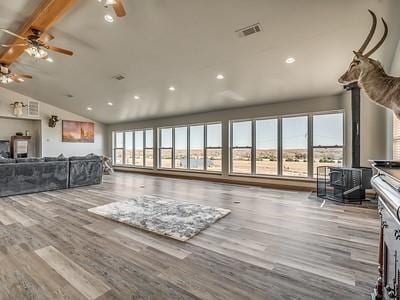 living room with beamed ceiling, light wood-type flooring, a wood stove, and high vaulted ceiling