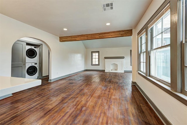 unfurnished living room featuring dark wood-type flooring, plenty of natural light, stacked washing maching and dryer, and vaulted ceiling with beams