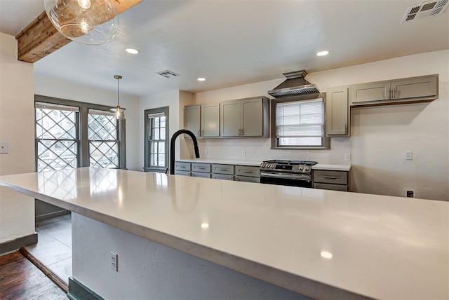 kitchen featuring pendant lighting, gray cabinetry, exhaust hood, stainless steel stove, and kitchen peninsula