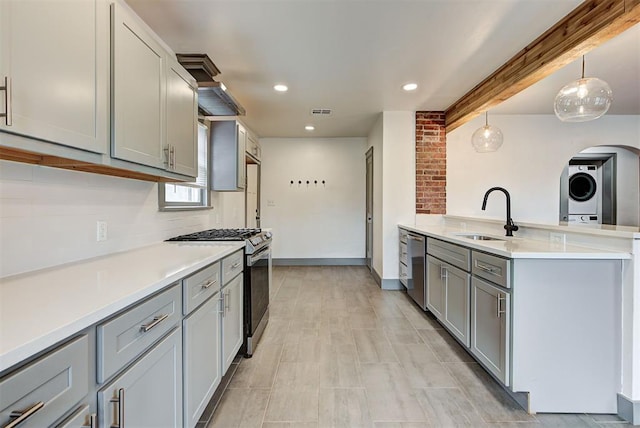 kitchen with gray cabinetry, stainless steel appliances, sink, decorative light fixtures, and stacked washer / drying machine